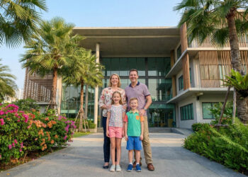 Une famille souriante devant un bâtiment moderne d'école internationale entouré de palmiers et de fleurs en Thaïlande.