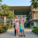 Une famille souriante devant un bâtiment moderne d'école internationale entouré de palmiers et de fleurs en Thaïlande.