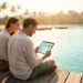 Un couple souriant regarde une tablette sur un ponton en bois au bord d'une mer tropicale avec des temples en arrière-plan.