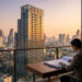 Un homme en costume étudie des plans architecturaux sur un bureau avec une vue panoramique sur les gratte-ciels de Bangkok.