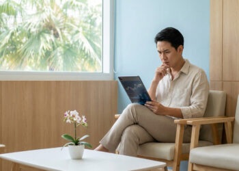 Homme asiatique inquiet consultant des données financières sur une tablette dans une salle d'attente.