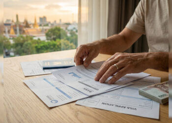 Mains d'un homme examinant des documents bancaires et un formulaire de visa avec une vue sur Bangkok en arrière-plan.
