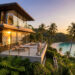 Un homme se tient sur la terrasse d'une villa moderne surplombant une plage tropicale au coucher du soleil à Phuket.
