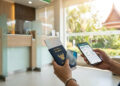 Mains tenant un passeport thaïlandais, une carte bancaire et un smartphone dans une agence bancaire.