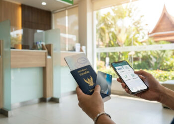 Mains tenant un passeport thaïlandais, une carte bancaire et un smartphone dans une agence bancaire.