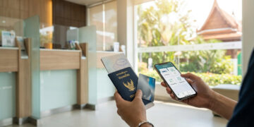 Mains tenant un passeport thaïlandais, une carte bancaire et un smartphone dans une agence bancaire.