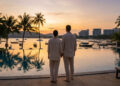 Un couple debout devant une piscine à débordement contemplant un coucher de soleil sur une plage thaïlandaise.