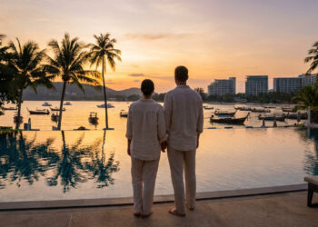 Un couple debout devant une piscine à débordement contemplant un coucher de soleil sur une plage thaïlandaise.