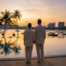 Un couple debout devant une piscine à débordement contemplant un coucher de soleil sur une plage thaïlandaise.