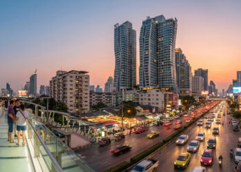 Une passerelle piétonne surplombant une rue animée de Sukhumvit à Bangkok au coucher du soleil avec des gratte-ciels.