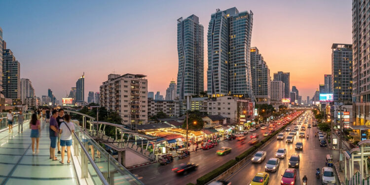 Une passerelle piétonne surplombant une rue animée de Sukhumvit à Bangkok au coucher du soleil avec des gratte-ciels.
