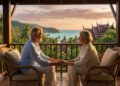 Couple de seniors se tenant la main sur une terrasse en Thaïlande au coucher du soleil avec vue sur la mer.