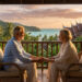 Couple de seniors se tenant la main sur une terrasse en Thaïlande au coucher du soleil avec vue sur la mer.