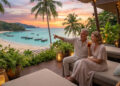 Couple de retraités admirant un coucher de soleil tropical sur une plage thaïlandaise depuis une terrasse luxueuse.