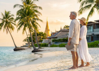 Un couple de retraités avec une tablette sur une plage thaïlandaise au coucher du soleil.