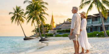 Un couple de retraités avec une tablette sur une plage thaïlandaise au coucher du soleil.