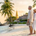 Un couple de retraités avec une tablette sur une plage thaïlandaise au coucher du soleil.
