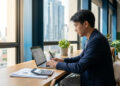 Un homme en costume travaillant sur un ordinateur portable dans un bureau moderne avec vue sur la ville.