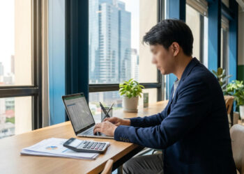 Un homme en costume travaillant sur un ordinateur portable dans un bureau moderne avec vue sur la ville.