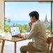 Un homme travaillant sur un ordinateur portable dans un salon moderne avec vue sur la mer et un temple en arrière-plan.