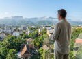 Un homme sur un balcon surplombant Chiang Mai avec une tablette, analysant des données immobilières.