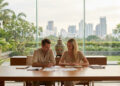 Couple expatrié discutant de documents juridiques devant une fenêtre donnant sur la skyline de Bangkok.