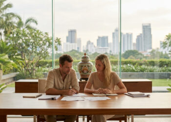 Couple expatrié discutant de documents juridiques devant une fenêtre donnant sur la skyline de Bangkok.