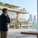 Un homme en costume regarde un écran transparent affichant un diagramme de flux complexe devant un campus moderne.