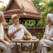 Trois retraités discutent et sourient autour d'une table sur une terrasse en Thaïlande.