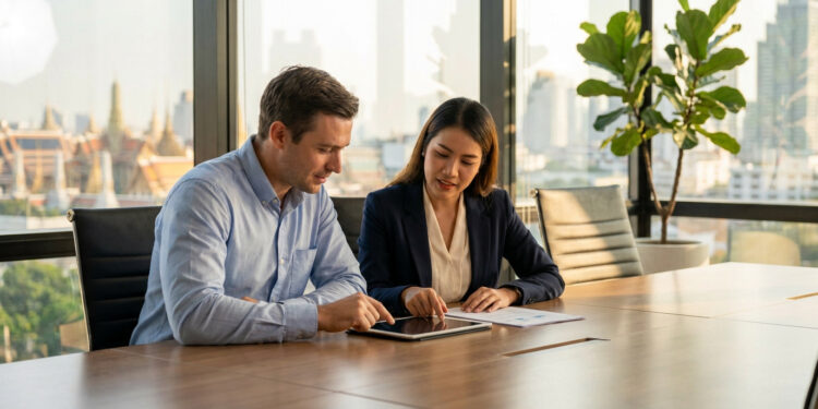 Homme et femme d'affaires collaborant sur une tablette dans un bureau avec vue sur Bangkok.