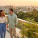 Un couple heureux se tenant la main sur une terrasse avec une vue panoramique sur une ville au coucher du soleil.