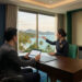 Un homme en costume utilisant une tablette devant une employée dans un bureau de luxe avec vue sur la mer en Thaïlande.