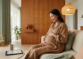 Une femme enceinte souriante assise sur un canapé, consultant une tablette pour préparer son accouchement.