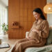 Une femme enceinte souriante assise sur un canapé, consultant une tablette pour préparer son accouchement.