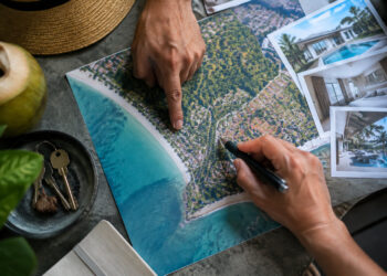 Mains examinant une carte aérienne d'une côte thaïlandaise et des photos de villas pour un projet immobilier.
