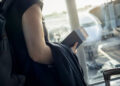 Une personne avec un sac à dos tenant un passeport et un billet d'avion face à un avion sur le tarmac d'un aéroport.