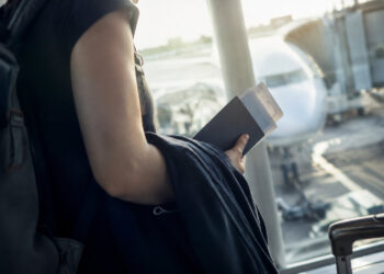 Une personne avec un sac à dos tenant un passeport et un billet d'avion face à un avion sur le tarmac d'un aéroport.