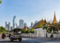 Un tuk-tuk roule sur une route de Bangkok avec, en arrière-plan, un temple traditionnel et des gratte-ciels modernes.