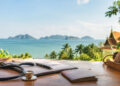 Stéthoscope, stylo et passeport posés sur une table en bois face à un paysage tropical avec vue sur la mer.