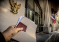 Une main tient des dossiers devant l'entrée d'un bâtiment officiel en Thaïlande avec le symbole du Garuda au mur.