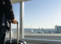 Un voyageur tenant une valise à roulettes dans un aéroport, regardant les avions sur le tarmac.