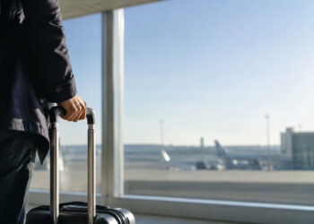 Un voyageur tenant une valise à roulettes dans un aéroport, regardant les avions sur le tarmac.