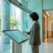 Une femme utilisant une borne interactive pour un bilan de santé dans un hôpital moderne avec vue sur la ville.