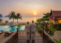 Couple âgé admirant un coucher de soleil sur une plage en Thaïlande depuis la terrasse d'une villa de luxe.