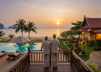 Couple âgé admirant un coucher de soleil sur une plage en Thaïlande depuis la terrasse d'une villa de luxe.
