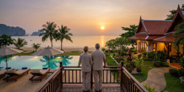 Couple âgé admirant un coucher de soleil sur une plage en Thaïlande depuis la terrasse d'une villa de luxe.