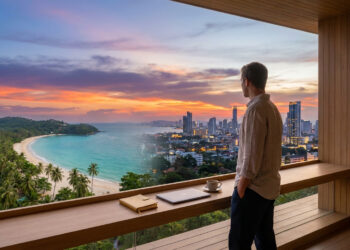 Un homme regarde un coucher de soleil sur une plage tropicale et une ville depuis un bureau moderne avec ordinateur.