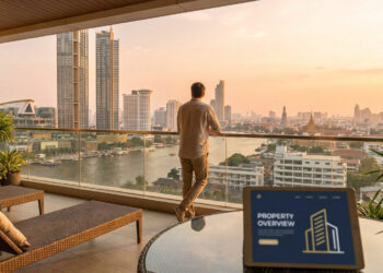 Un homme sur un balcon surplombant Bangkok avec une tablette affichant une application immobilière au premier plan.